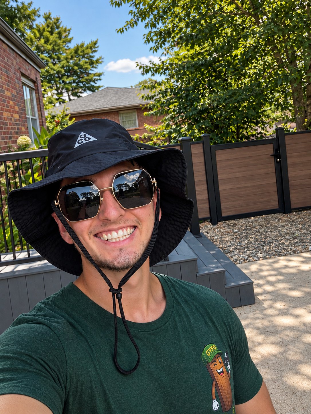 Devon, the owner of Get Your Fence On, on site in a company shirt with a finished composite fence and gate behind him