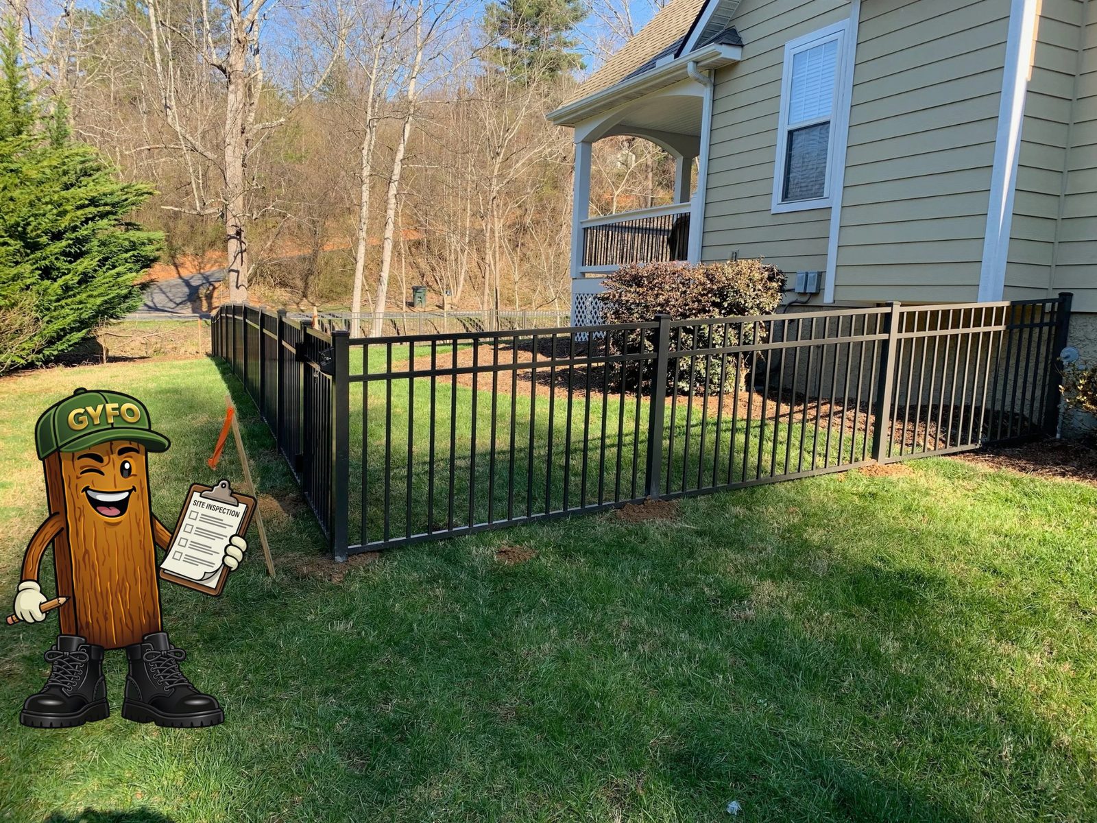 Black aluminum fence wrapping a yard beside a tan house, the GYFO mascot checking a site-inspection clipboard - a Get Your Fence On install