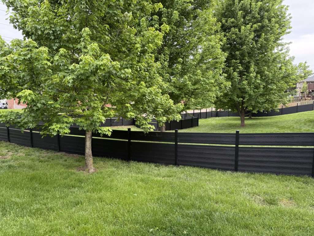 Dark horizontal fence with a narrow open band around a lawn with mature trees.