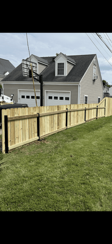 Back of a wood picket fence showing horizontal rails and dark posts beside a lawn.