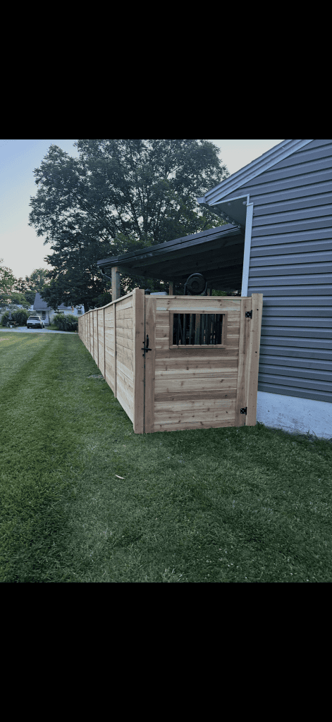 Horizontal wood fence and matching gate with a black picket insert beside a house.
