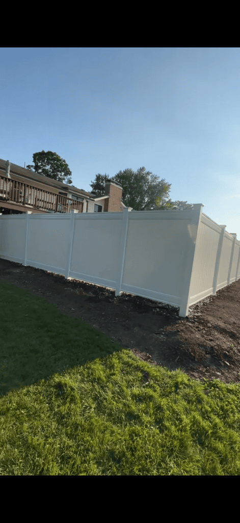 White privacy fence turning a corner behind a house, viewed across the grass.