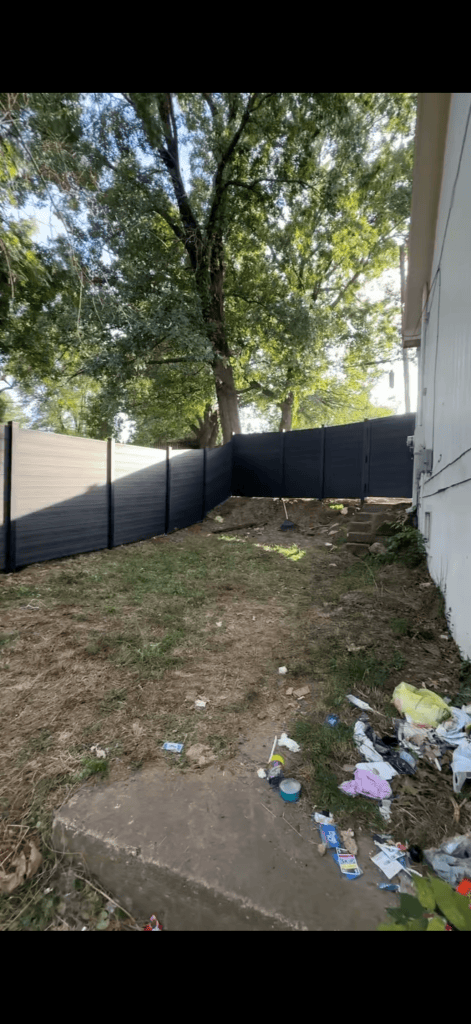 Gray privacy panels along a side yard, meeting a darker fence beneath a large tree.