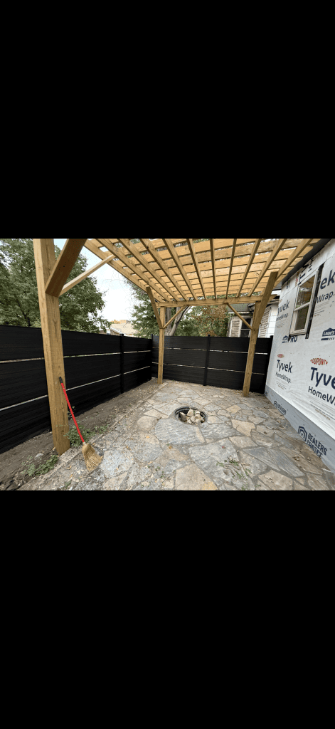 Dark horizontal privacy screens enclosing a stone patio beneath an open timber roof frame.