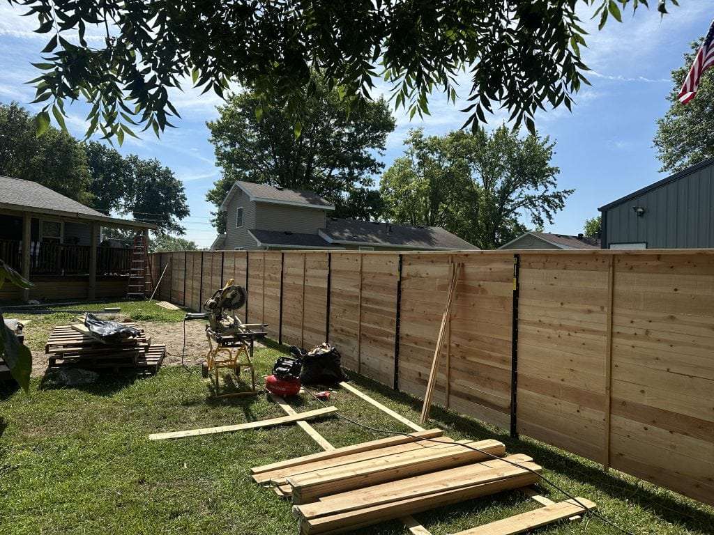 Horizontal wood privacy fence under construction, with boards and tools laid out on the grass.