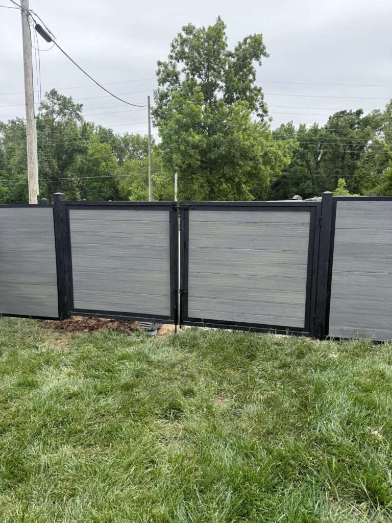Gray horizontal-panel gate with black framing in a matching fence beside a lawn.