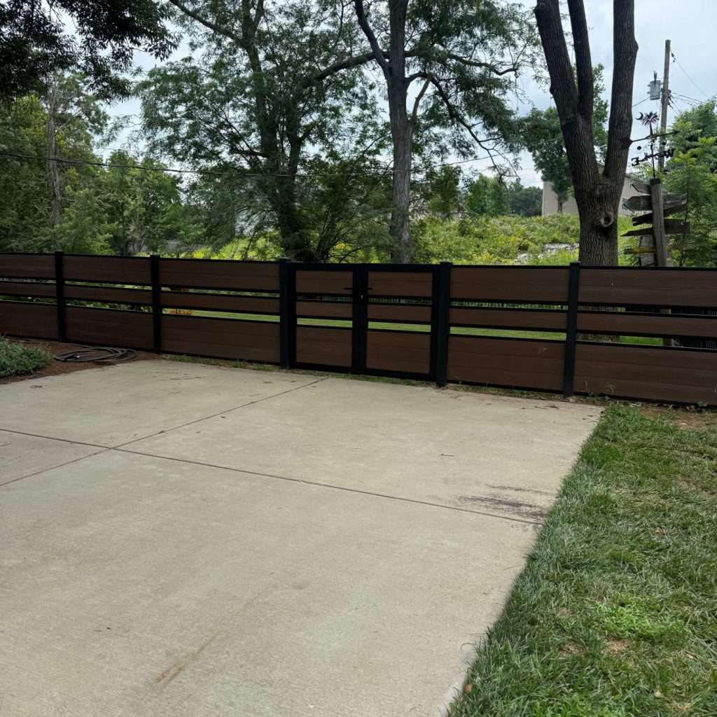 Brown horizontal fence enclosing a concrete patio beneath trees.
