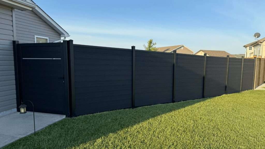 Dark horizontal privacy fence and walk gate beside a house on a sloping lawn.