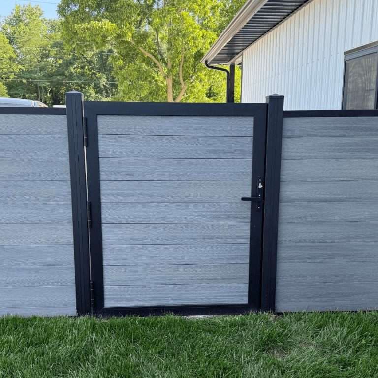 Gray horizontal-panel walk gate in a matching fence beside a lawn and outbuilding.