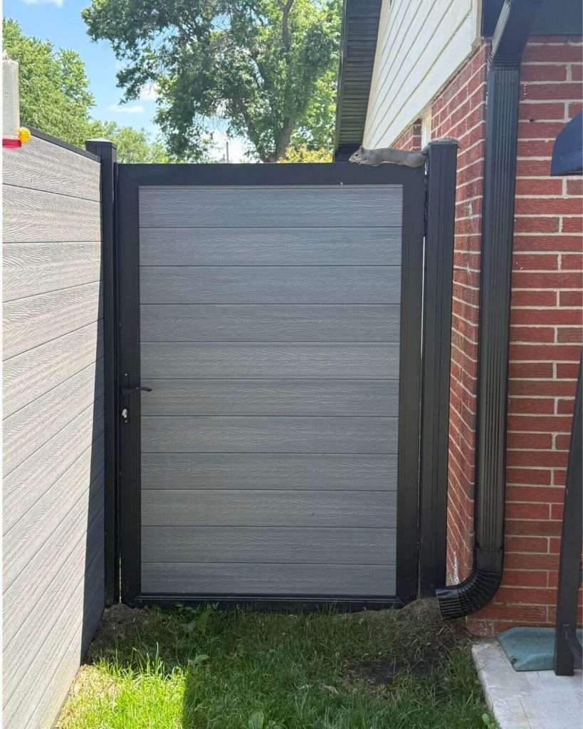Gray horizontal-panel walk gate with black framing in a narrow passage between buildings.