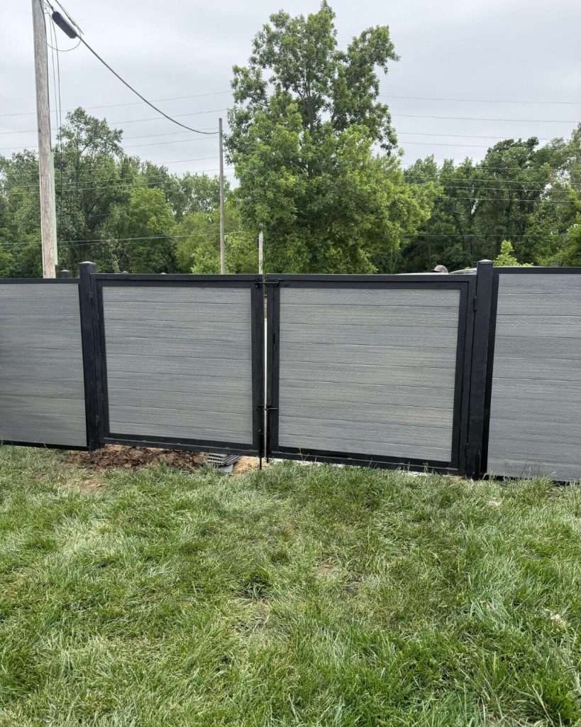 Gray horizontal-panel gate with black framing in a matching fence beside a lawn.