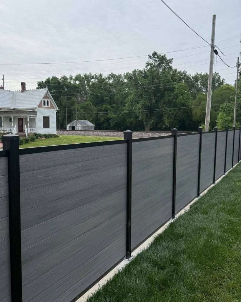 Gray horizontal fence with stepped top edges and black posts following a sloped lawn.