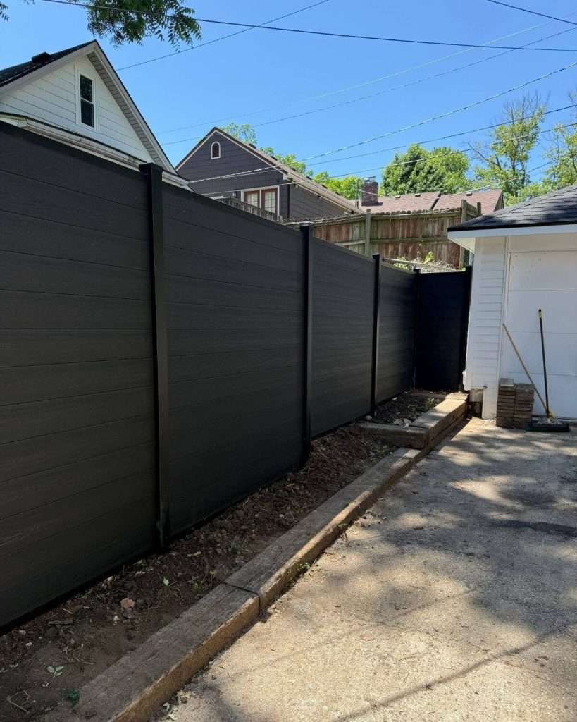Dark privacy panels beside a paved area leading to a white garage.