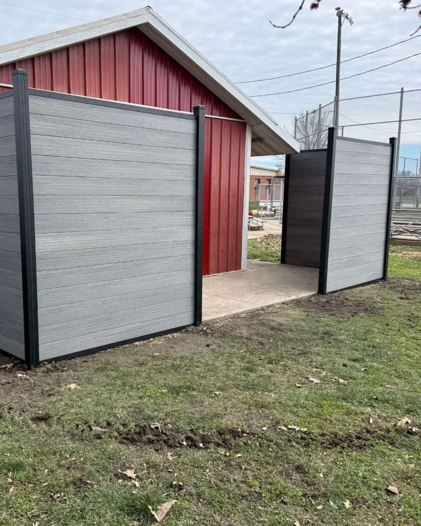 Gray horizontal fence and an open gate beside a red outbuilding.