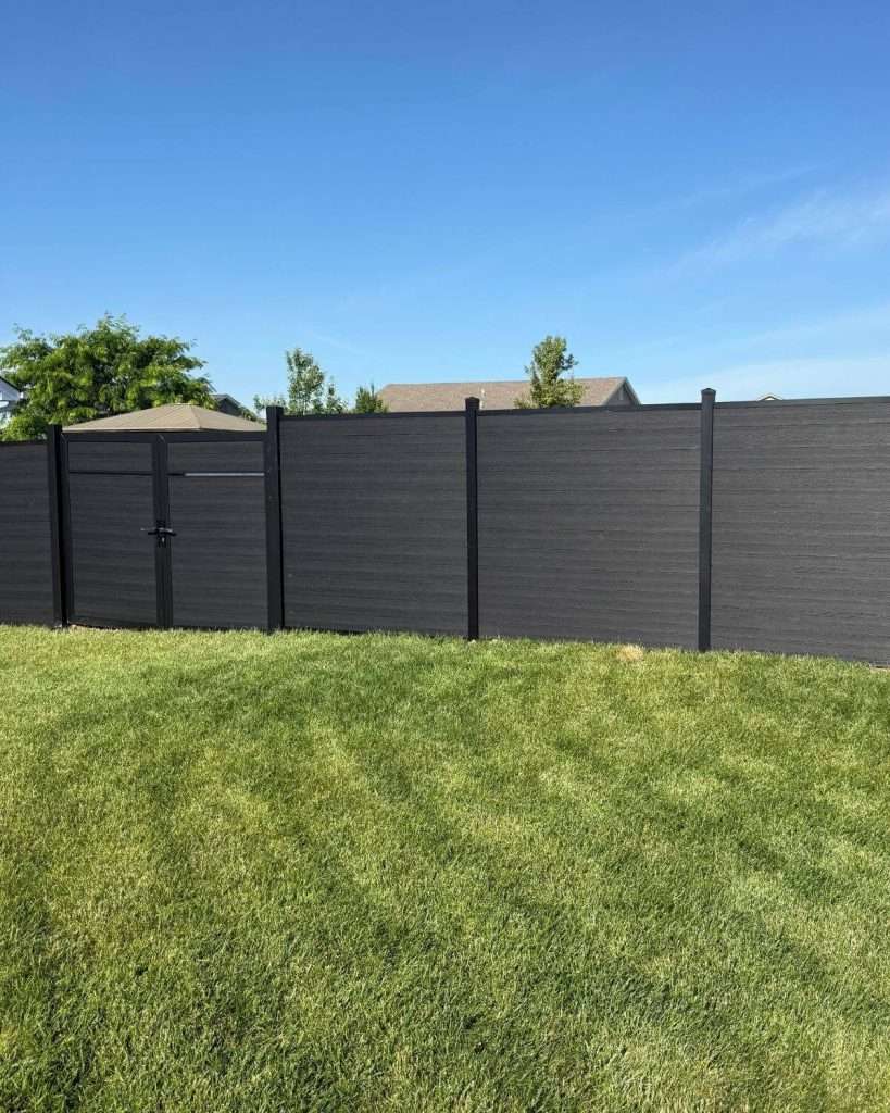 Dark horizontal privacy fence with a gate across a grass yard.