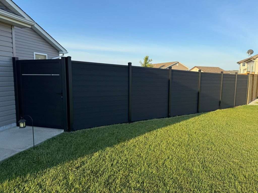 Dark horizontal privacy fence and walk gate beside a house on a sloping lawn.