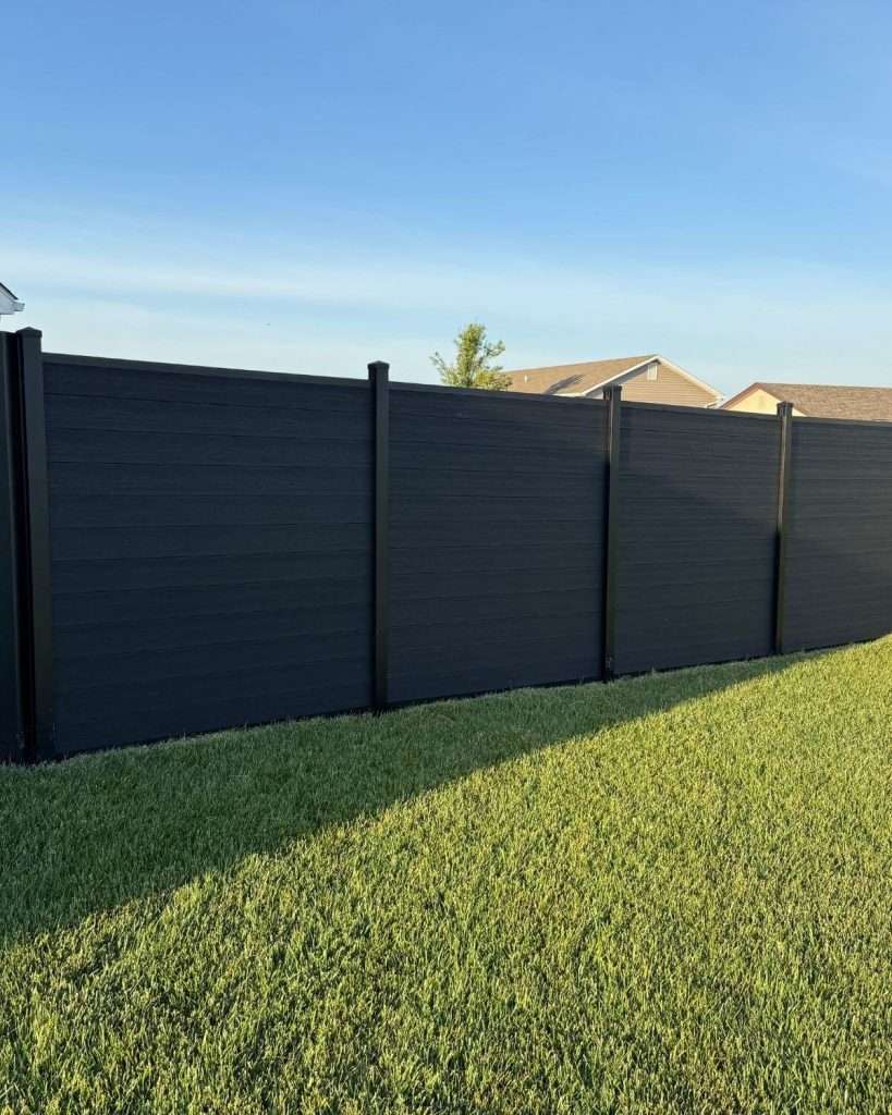 Dark horizontal privacy panels along a sunlit grass yard, viewed at an angle.