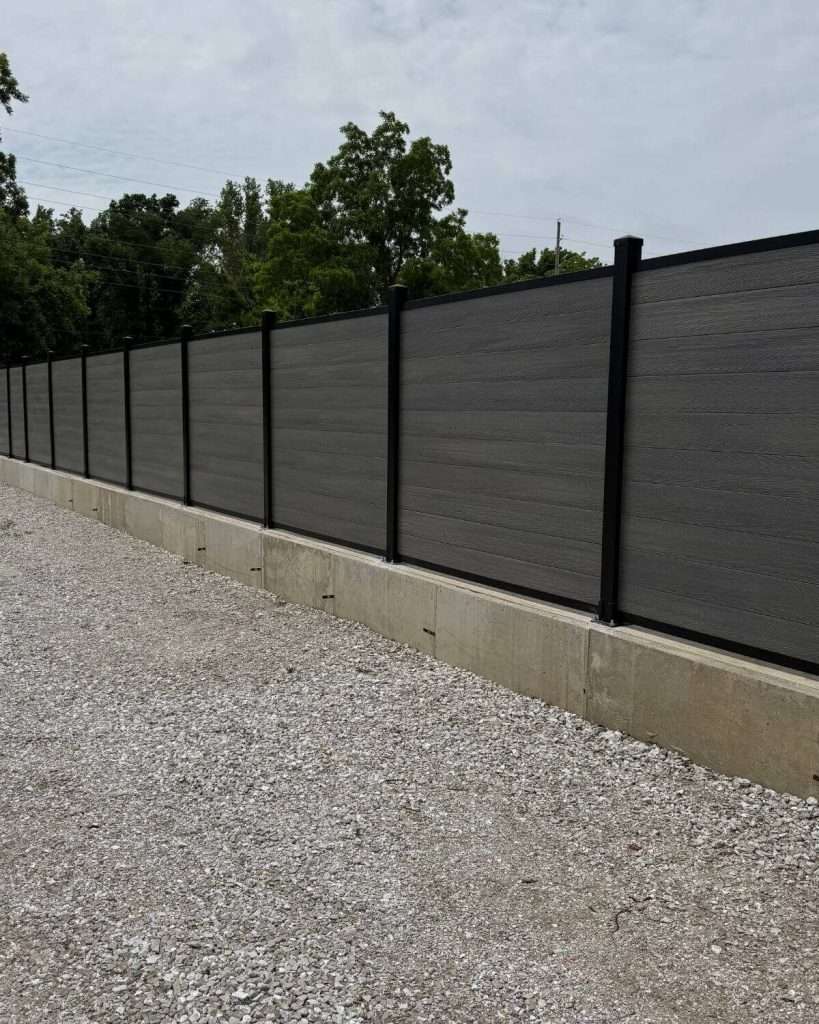 Gray horizontal panels above a concrete curb along a gravel area.