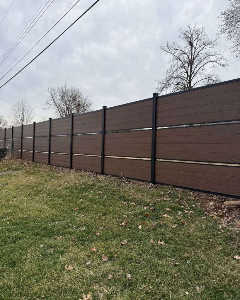 Brown horizontal fence with narrow gaps and dark posts following a rising lawn.
