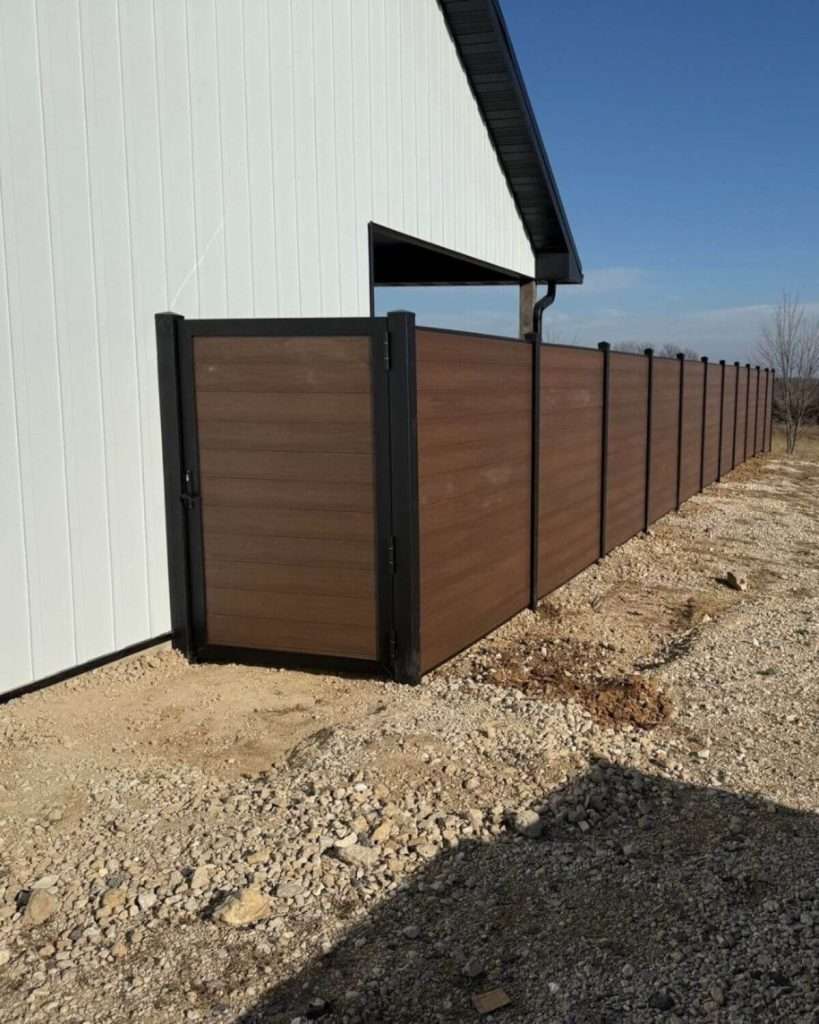 Brown horizontal privacy fence and walk gate alongside a light-colored outbuilding on gravel.