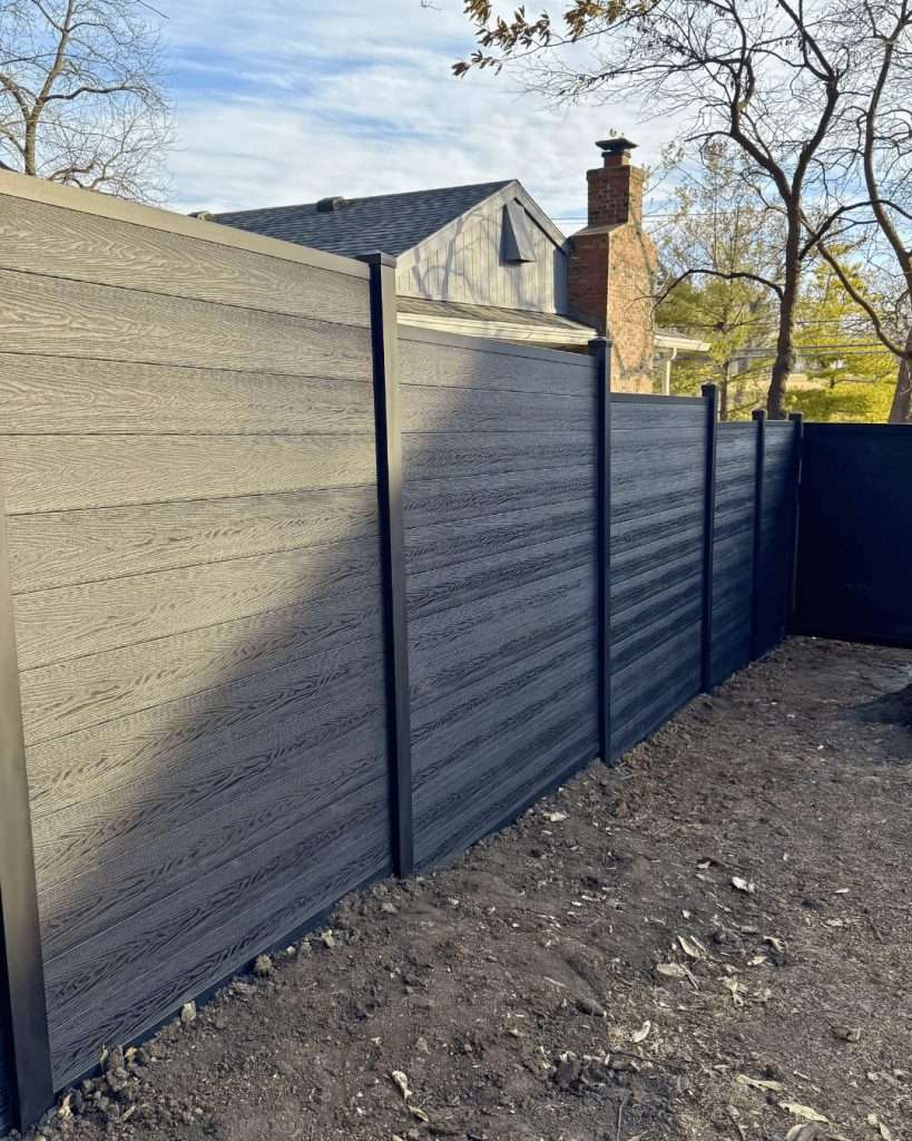 Close view of textured dark horizontal privacy panels and black posts beside bare ground.