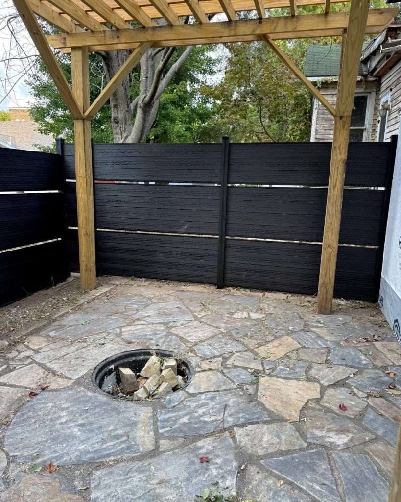 Dark horizontal privacy screens around a stone patio with a fire pit beneath a timber pergola.