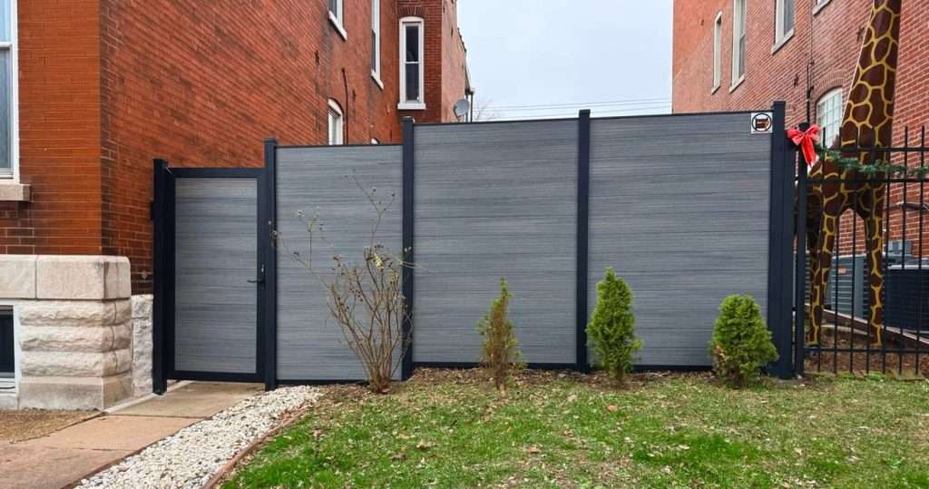 Gray horizontal privacy panels and a walk gate between brick buildings.